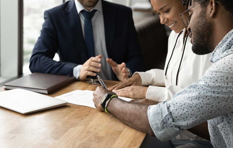A person holding a mortgage pre-approval letter while viewing house listings on a tablet at a kitchen table.